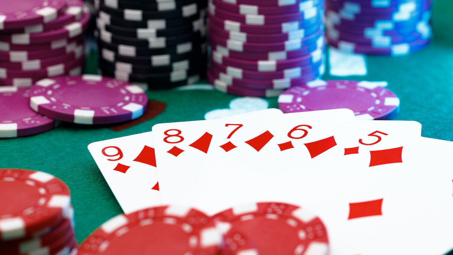 Zum großen Spiel gehören Roulette, Poker, Black Jack und Würfelspiele Auf einem grünen Kasinotisch liegen Spielkarten und Jetons.